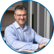 Retrato profissional em close-up circular de consultor ou gestor sênior sorrindo, com óculos e camisa azul, ideal para a seção 'Nossa Equipe' ou 'Liderança'.